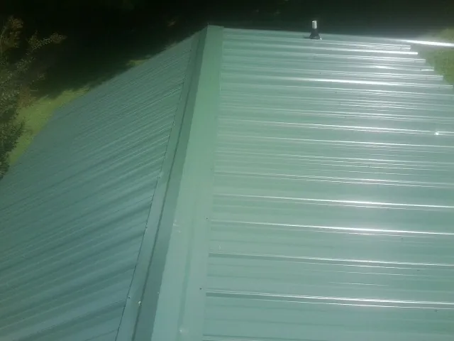 New green metal panels meeting at the ridge of a roof — Flat Roof Repair work by our crew in Hamden