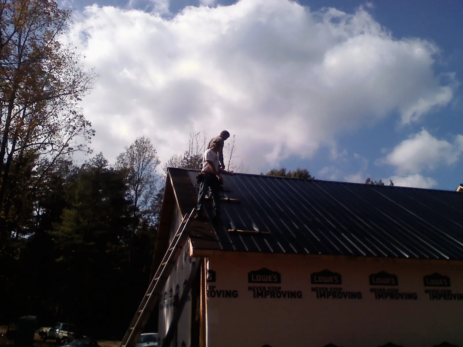 Roofer fastening dark metal panels high against a cloudy sky, from a Roof Inspection job in Hamden
